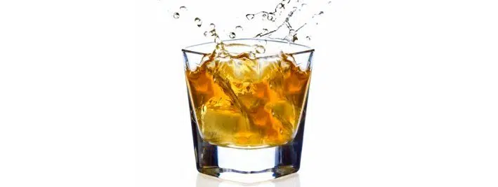 Ice cube splashing into a snifter of scotch.